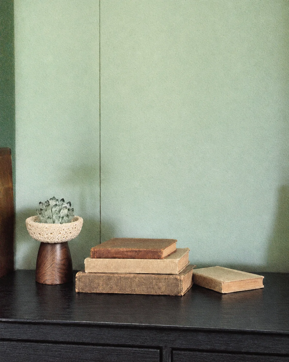 Crystal incense bowl beside stacked books on a green wall
