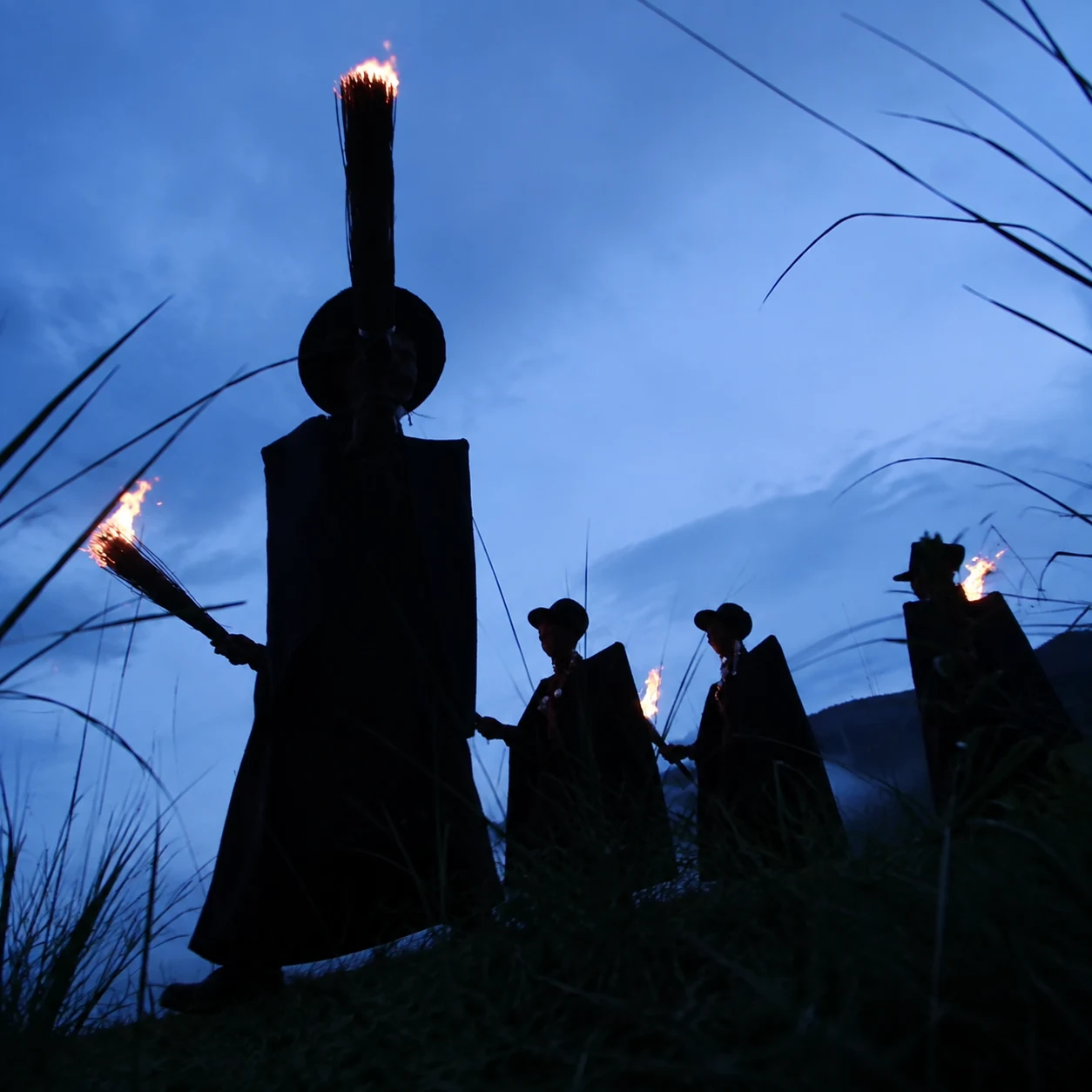 Yi ceremonial figures carrying torches across a hillside at blue hour