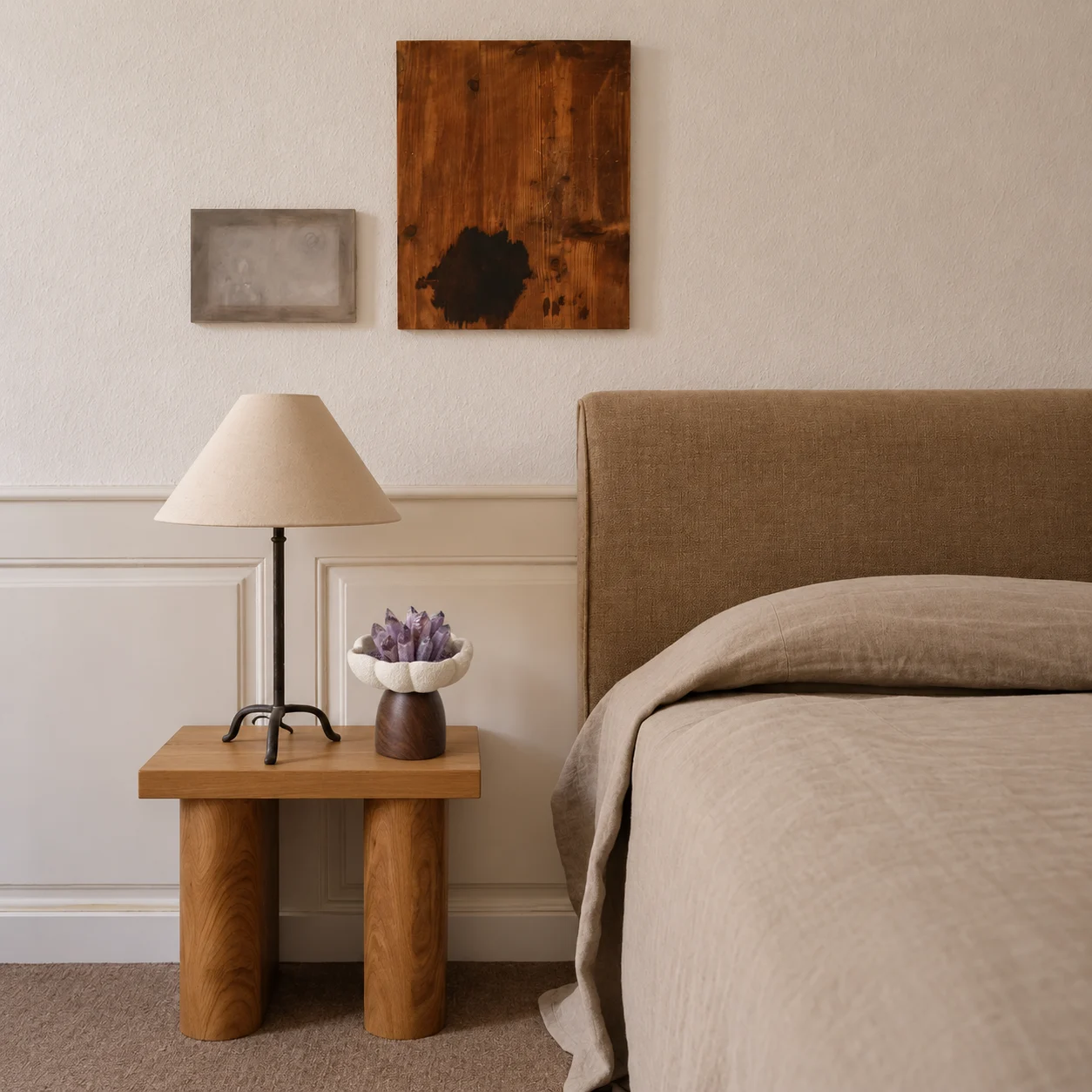 Amethyst ornament beside a lamp on a wooden bedside table in a quiet linen bedroom