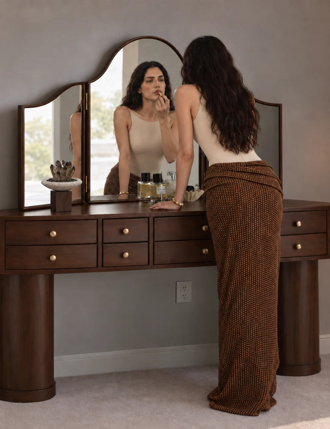Woman preparing at a walnut dressing table with a yellow crystal bracelet and smoky quartz ornament