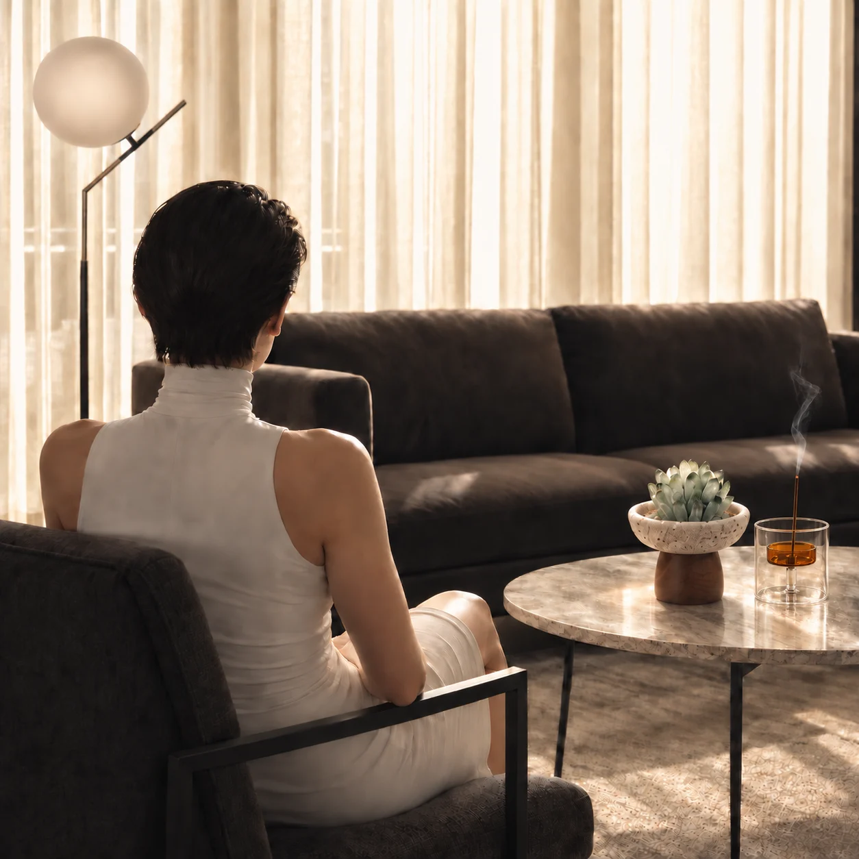 Woman resting in a sunlit living room with a green crystal ornament and amber glass incense holder on a marble table