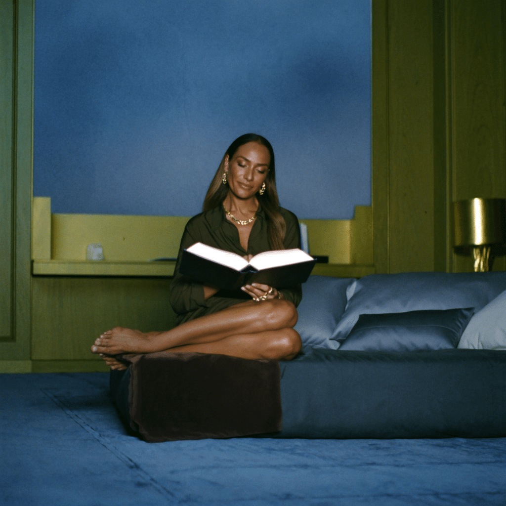 A woman reading a book on a bed in a blue and olive interior.