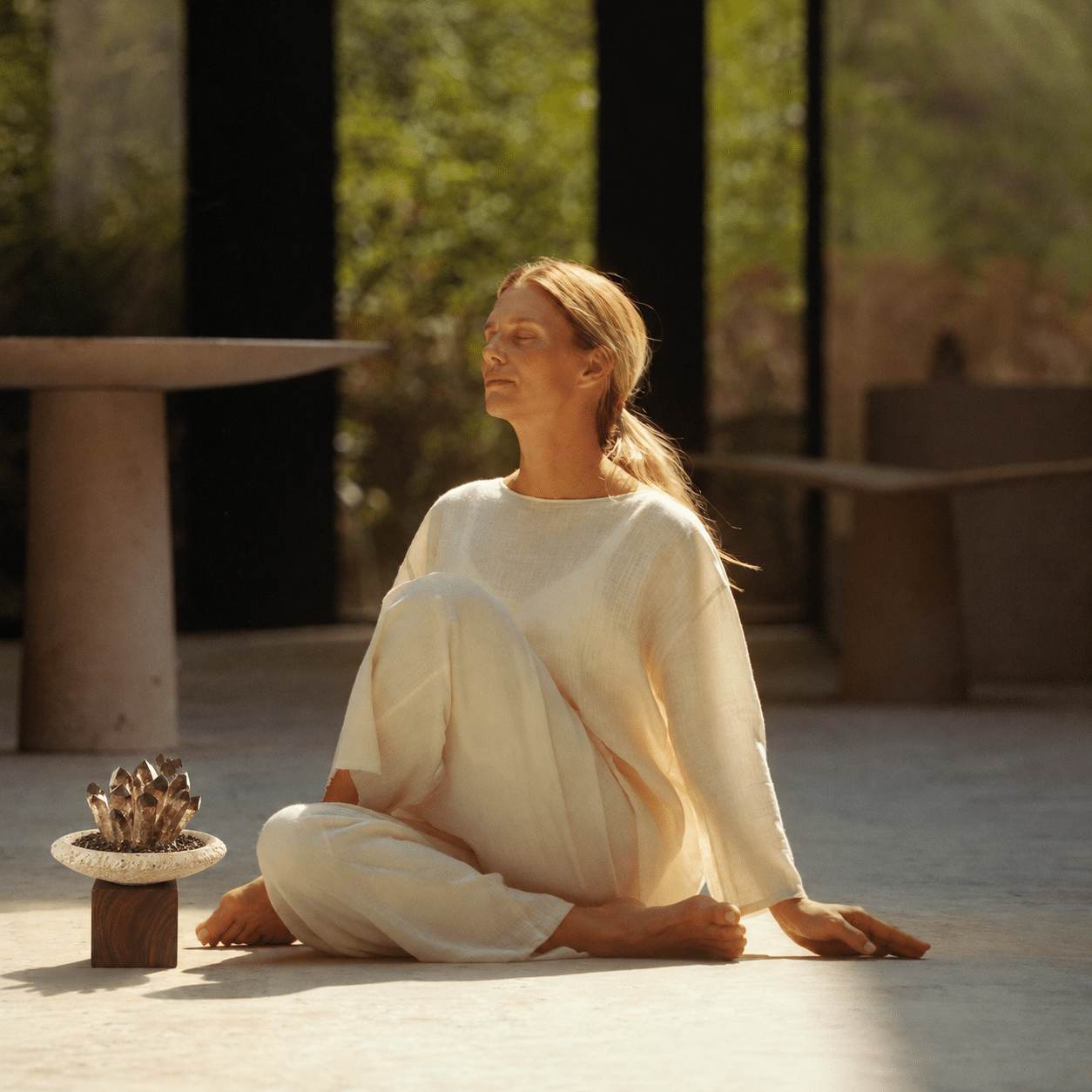Woman meditating in warm sunlight beside a smoky crystal bowl